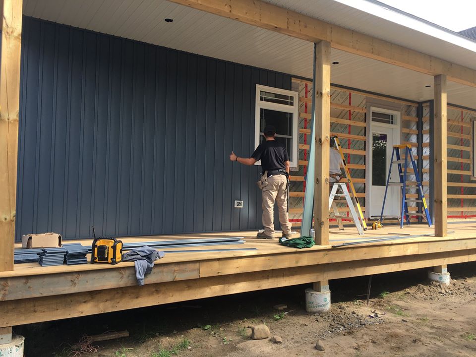 man in black shirt and beige pants working on the siding of a home