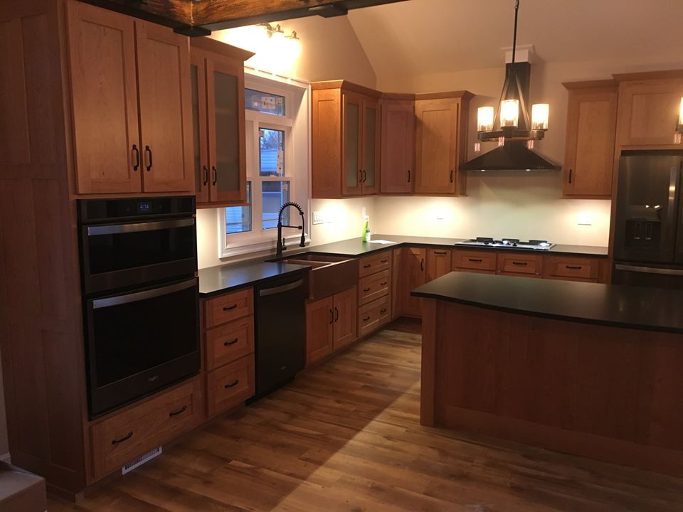 a renovated kitchen with black countertops and brown wood cabinetry