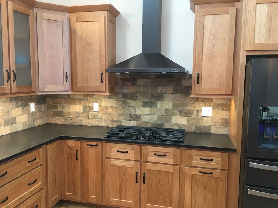 a renovated kitchen with black countertops and brown wood cabinetry