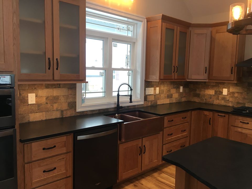 a renovated kitchen with black countertops and brown wood cabinetry